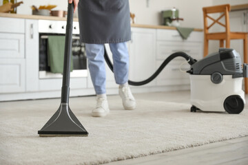 Young woman hoovering carpet in kitchen, closeup