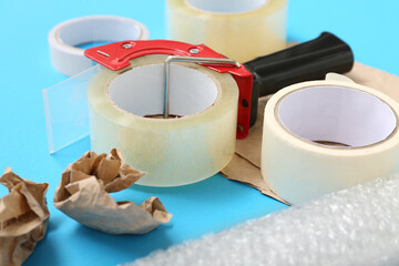 Adhesive tape rolls, dispenser, bubble wrap and paper on blue background