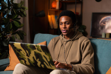 Delghted attractive dark skinned man at cozy home sitting in the living room wearing wireless...