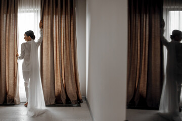 young beautiful bride in white pajamas in the morning. The bride's morning at the hotel. Long fashionable veil. Mirror photo