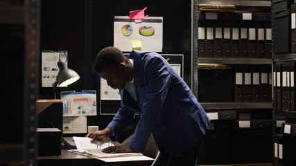 Focused african american agent meticulously examines evidence, researches records, and gathers...