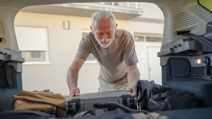 One senior man travel concept male put suitcase in trunk of the car