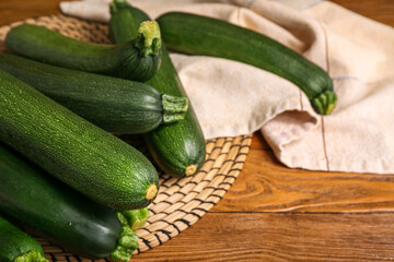 Wicker mat with many fresh zucchini on brown wooden background