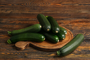 Board with many fresh zucchini on brown wooden background