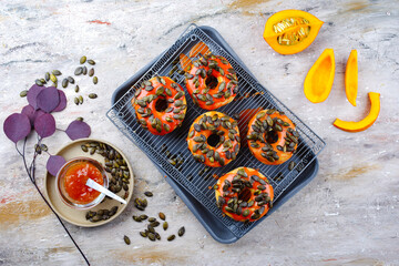Traditional American autumn donuts garnished with pumpkin seeds and pumpkin glaze and served as top view on a baking tray with grid