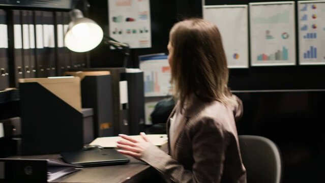 Female private investigator stands and walks out of the office while carrying laptop bag. Caucasian police officer closes her personal computer and arranges workstation leaving for the day.