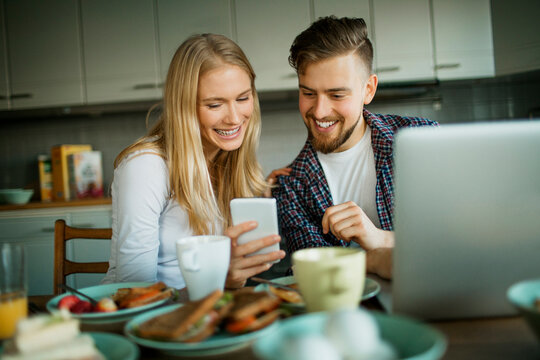 Young Caucasian couple using a smartphone while having breakfast in the kitchen