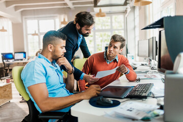 Diverse group of male colleagues going through paperwork while working on project in a marketing...