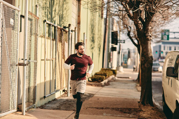 Fototapeta na wymiar Young Caucasian man jogging on a sidewalk in the the city in the US
