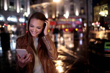 Young Caucasian woman using a smartphone on the sidewalk in London UK at night