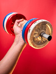 Hand carrying a colorful dumbbell on red background