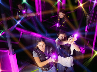 Laser tag players cheerful positive smiling guys and girls playing in teams in dark laser tag room. View from above