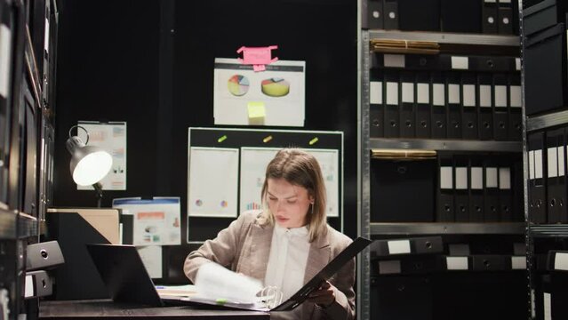 Dedicated female private detective accurately conducts research for clues and information. Using technology in office room, caucasian police officer examines evidence files and does forensic analysis.