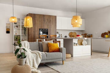 Interior of modern open plan kitchen with island table, grey sofa and glowing lamps - Powered by Adobe