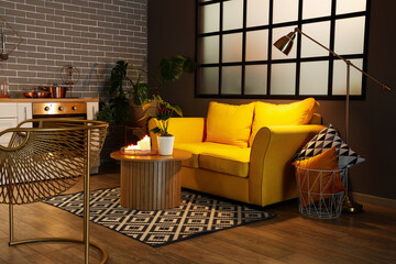 Interior of modern kitchen with glowing lamps, burning candles and yellow sofa at evening