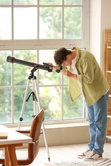 Young man using telescope at home