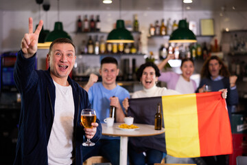 Emotional company of young adult fans supporting Belgian team with state flag while resting in...