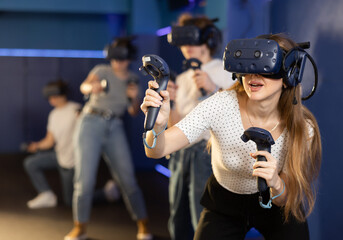 indoors, girl in virtual reality headset with joysticks in her hands actively moves and gesticulates while playing fighting game. Immersive Technologies XR VR AR MR © JackF