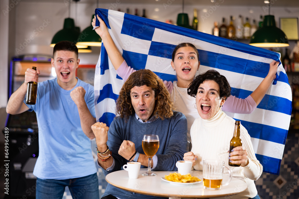 Wall mural group of emotive friends supporters cheering for favorite team with flag of greece while watching ma