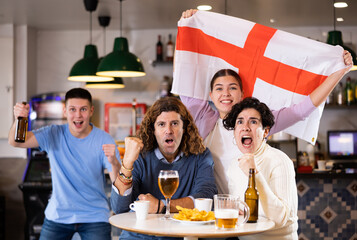 Group of friends, sports supporters cheering for favorite team with flag of England while watching...