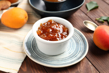 Bowl with sweet apricot jam on wooden background