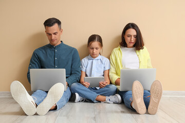 Family involved with gadgets sitting near beige wall