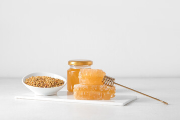 Board with bowl of bee pollen, honey and combs on light background