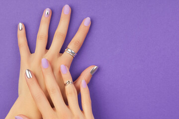 Beautiful groomed womans hands with matte lavender nail design on purple background. Manicure,...