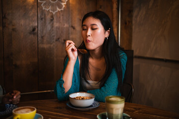 Asian young woman enjoying a tasty acai bowl at a cafeteria. Brunch concept.