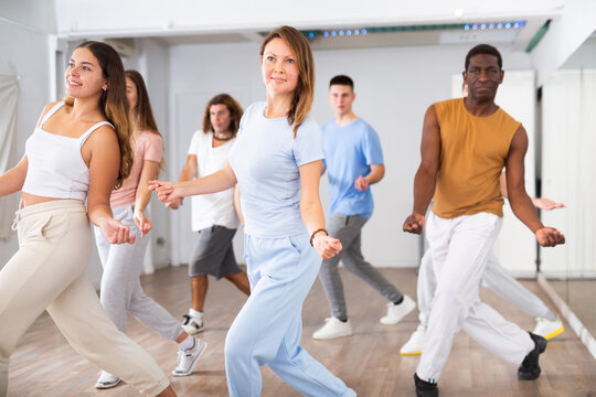 Class of active young adult dancers performing steps during exercising modern dance together in dance hall