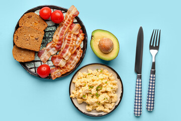 Plates of tasty scrambled eggs and bacon on blue background