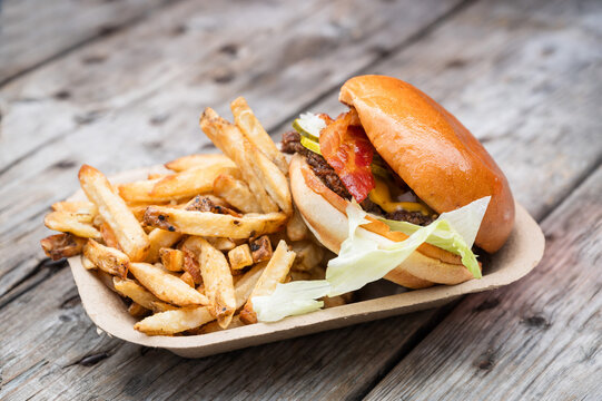 A take away bacon cheese burger with fresh fries.  Served in a compostable paper tray.