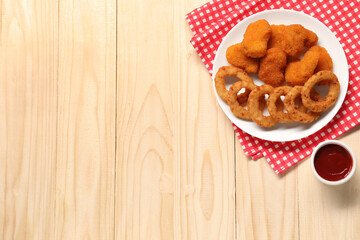 Tasty fried onion rings, chicken nuggets and ketchup on wooden table, flat lay. Space for text