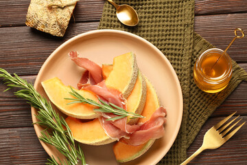 Composition with tasty melon, prosciutto, rosemary and honey on dark wooden background
