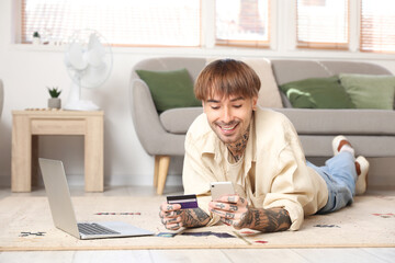 Tattooed young man with credit card using mobile phone at home