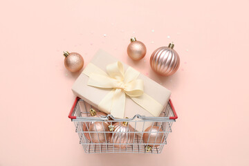 Small shopping basket with Christmas balls and gift box on beige background