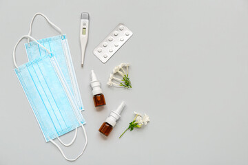 Bottles of nasal drops with medical masks, pills and thermometer on grey background