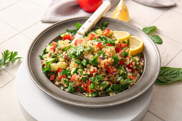 Plate with delicious tabbouleh salad on light tile background, closeup