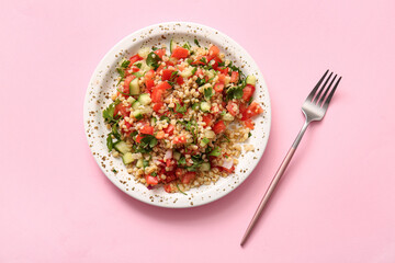 Plate with delicious tabbouleh salad and fork on pink background