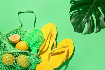Composition with mesh bag, fresh lemons, stylish flip flops and portable electric fan on green...