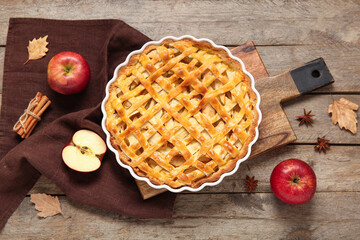 Baking dish with delicious apple pie and ingredients on wooden background