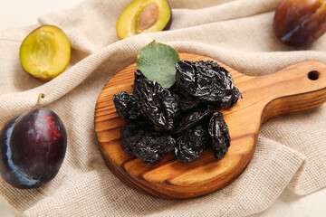 Wooden board with tasty dried plums on white background