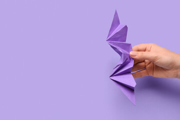 Female hand with origami bat on purple background