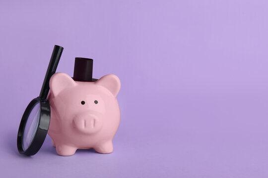 Piggy bank in top hat with magnifying glass on lilac background