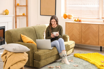 Young woman with cup of tea and laptop sitting at home on autumn day