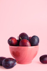 Bowl with fresh ripe plums on pink background