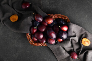 Wicker basket with fresh ripe plums on black background