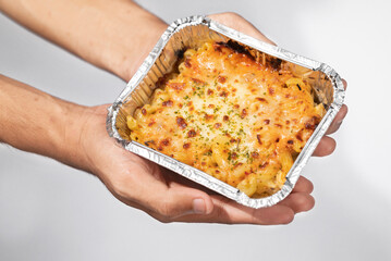 A human hand holding pasta macaroni schotel in an aluminum foil cup