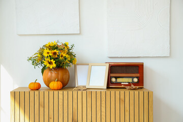 Pumpkins with autumn bouquet, blank frames and retro radio receiver on commode in room