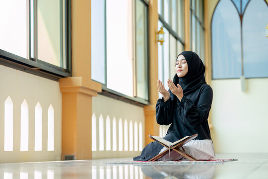 The image of an Asian Muslim woman in the Islamic religion in hijab in black color. Sitting reading the Quran and having a happy smiling face Staying in a beautiful mosque out of respect for God.